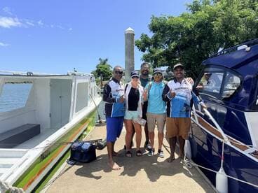 A cheerful group poses for a photo by their fishing boat, ready for an exciting day on the water. Perfect for fishing trips and group adventures.