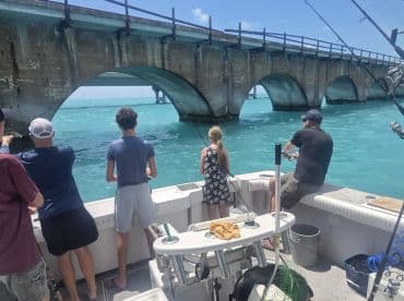 A group of anglers enjoys a fishing trip under a scenic bridge, casting lines into the vibrant turquoise waters — a perfect day for family fun on the boat.