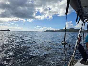 A scenic view from the side of a boat, showcasing the calm waters and distant islands under a partly cloudy sky — perfect for a day of sailing or exploring.