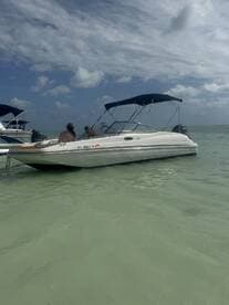 Two individuals relax on a boat in shallow waters, enjoying a sunny day on the water — perfect for a leisurely outing or beach day.