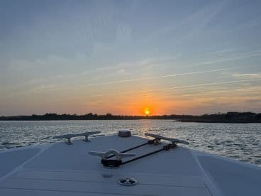 A serene sunset view from the bow of a boat, showcasing the tranquil waters and a picturesque horizon — perfect for evening cruises.