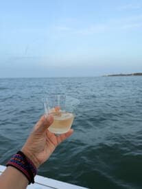 A hand holds a refreshing cocktail against the backdrop of serene waters, perfect for enjoying a relaxing day on the boat.