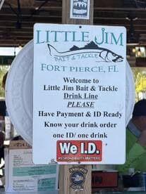 A sign at Little Jim Bait & Tackle in Fort Pierce, FL, detailing drink line procedures and ID requirements, with patrons visible in the background.