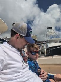 A father and son share a moment on a boat, both wearing sunglasses and enjoying their time together — perfect for family outings on the water.