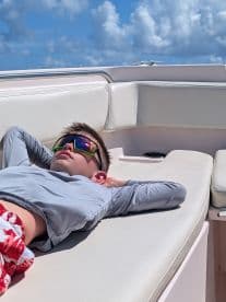 A young boy relaxes on the lounge area of a boat, enjoying the sun in stylish sunglasses — a perfect moment for leisure on the water.