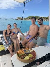 A cheerful group of friends enjoys a relaxing day on the boat, surrounded by stunning turquoise waters and a delicious spread of snacks — perfect for a fun day out on the water.