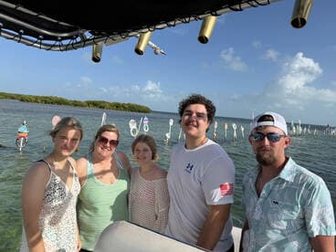 A cheerful group of friends poses for a photo on a boat, enjoying a beautiful day by the water with scenic views in the background.