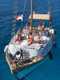 A lively group enjoys a sunny day aboard a boat, relaxing and sunbathing on the deck while surrounded by stunning blue waters.