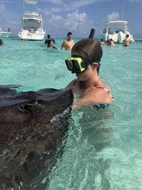 A child interacts closely with a stingray while snorkeling in clear waters, showcasing a unique wildlife experience in a tropical setting.