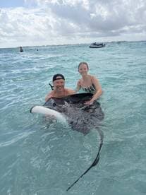 A joyful moment as a man and a girl interact with a stingray in shallow waters, showcasing a unique wildlife experience in the ocean.