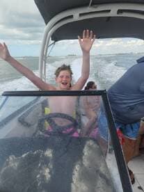 A joyful child enthusiastically steers a boat while surrounded by friends, capturing the excitement of a fun day on the water.