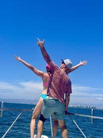 A joyful couple poses on the bow of a boat, celebrating their time on the water with a stunning ocean backdrop — perfect for memorable adventures and romantic getaways.