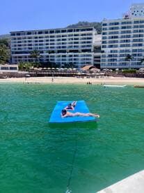 Two friends relax on a floating mat in the vibrant waters, enjoying a sunny day at the beach — a perfect scene for summer fun and relaxation.