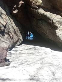 A couple stands silhouetted in a rocky cave, framed by the shimmering ocean beyond — a picturesque moment capturing the beauty of nature.