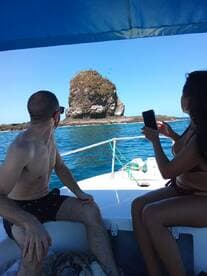 A couple enjoys a scenic boat ride, capturing the stunning rock formation in the distance — a perfect moment for adventure seekers exploring the coastline.