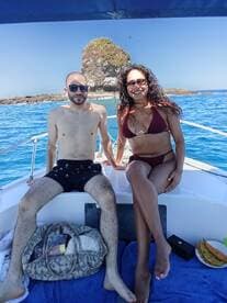A couple enjoys a sunny day on a boat, surrounded by beautiful tropical waters and a rocky island backdrop — perfect for romantic getaways or fun adventures at sea.