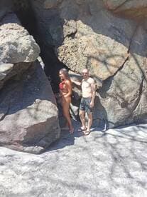 A couple poses playfully among the rocks at a sunny beach, capturing a moment of fun and adventure during their tropical getaway.