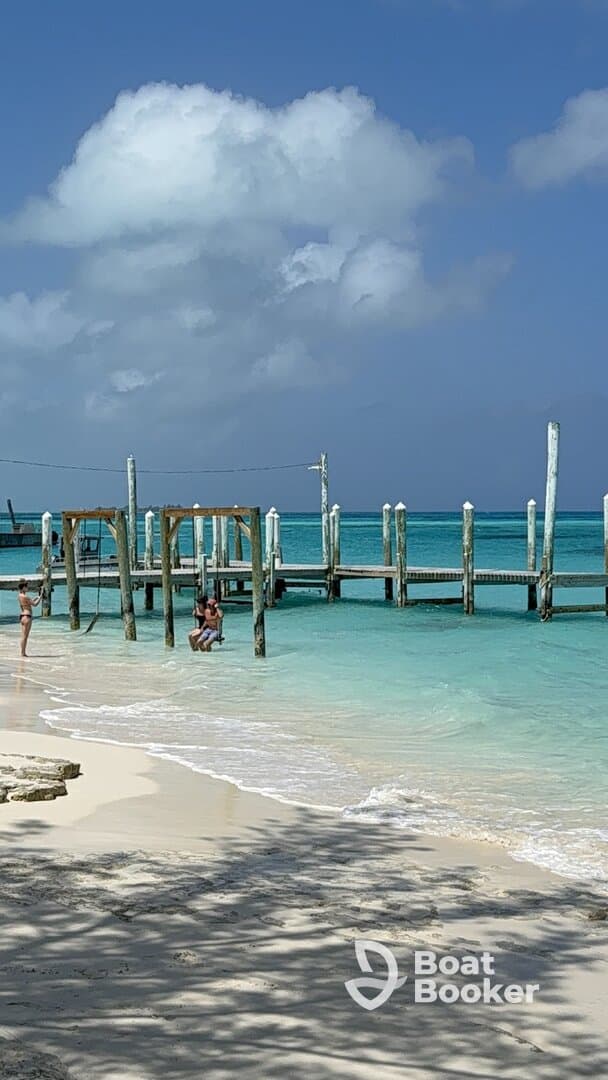 A couple enjoys a playful moment on a swing by the beach, with a picturesque pier and stunning turquoise waters in the background — a perfect scene for a tropical getaway.