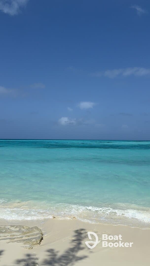 A serene view of turquoise waters meeting a sandy beach under a clear blue sky, perfect for showcasing tropical destinations.
