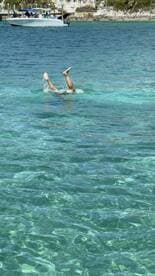 A person enjoys a playful moment in the clear turquoise waters, with a boat visible in the background, capturing the essence of a fun day on the water.