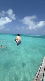 A young boy leaps into the crystal-clear turquoise waters, capturing the essence of summer fun and adventure in a tropical paradise.