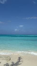 A serene view of turquoise waters meeting a sandy beach under a clear blue sky, perfect for showcasing tropical destinations.