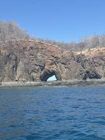 A stunning view of a natural rock arch along the coastline, showcasing the beauty of the surrounding waters and landscape — perfect for nature lovers and sightseeing tours.