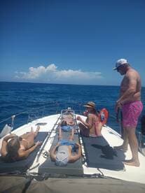 A group enjoys a relaxing day on the water, sunbathing on the deck of a boat under a clear blue sky — perfect for summer outings and fun in the sun.