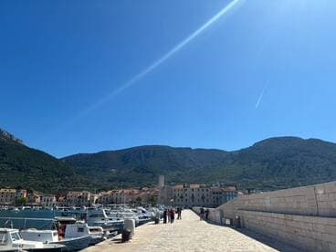 A picturesque harbor scene with boats lined up against the backdrop of stunning mountains and clear blue skies, perfect for exploring coastal destinations.