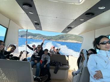 A lively group enjoys a boat ride, capturing fun moments with smiles and peace signs against a beautiful coastal backdrop.