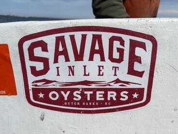 Close-up of the Savage Inlet Oysters logo on a boat, showcasing the brand from Outer Banks, NC.