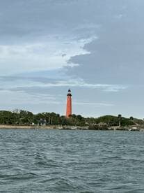 A picturesque view of a vibrant orange lighthouse standing tall along the coastline, surrounded by lush greenery and calm waters — a perfect representation of coastal charm.