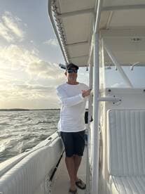 A man stands on the deck of a boat, enjoying the scenic views as the sun sets over the water — a perfect moment for boating enthusiasts.