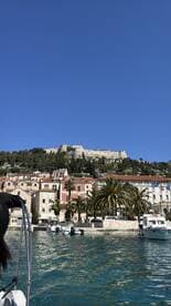 A picturesque view of a historic fortress overlooking a charming harbor, with palm trees and boats adding to the scenic beauty — perfect for exploring coastal destinations.