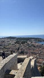 A stunning view of a coastal city with people exploring the historic fortifications, showcasing the beautiful architecture and serene waters of the harbor.