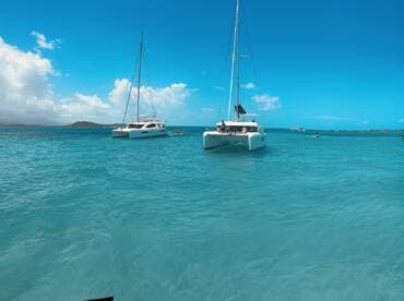 Two catamarans anchored in stunning turquoise waters, with guests enjoying the beautiful day — a perfect setting for sailing adventures and relaxation.
