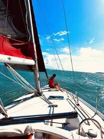 A serene moment on a sailboat with a person enjoying the ocean breeze under a clear blue sky — perfect for sailing enthusiasts and relaxation seekers.