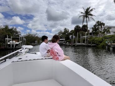 A young couple enjoys a serene moment on the bow of a boat, overlooking a tranquil waterway lined with palm trees — a perfect setting for relaxation and exploration.