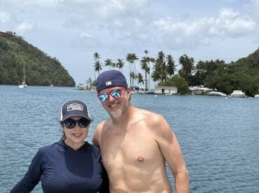 A cheerful couple poses against a scenic backdrop of palm trees and calm waters, capturing a perfect moment of joy on their boating adventure.