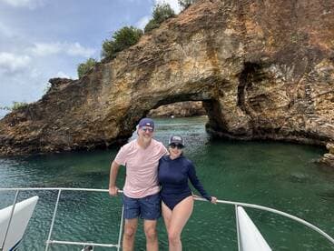 A couple poses on the bow of their boat with a stunning rock formation in the background, capturing a memorable moment during their aquatic adventure.