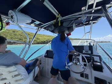 Inside view of a boat's helm with a captain at the wheel, showcasing the cabin's layout and equipment — perfect for navigating the beautiful turquoise waters.