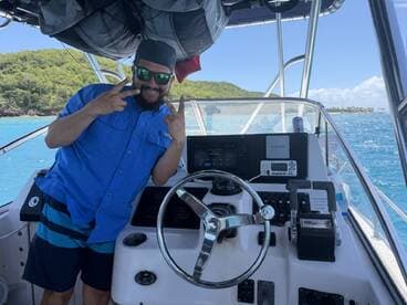 A cheerful captain poses at the helm of a boat, showcasing the console and steering wheel, perfect for navigating the beautiful waters.