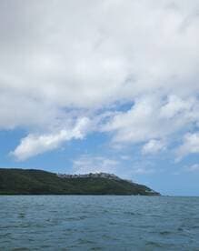 A scenic view of a lush coastline with buildings perched on the hillside, showcasing the beauty of the landscape from the water.