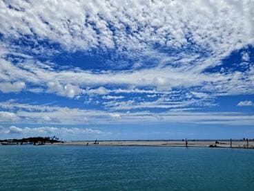 A stunning view of a sandy beach with people enjoying the sun, framed by a vibrant blue sky and fluffy clouds — a perfect destination for relaxation and fun in the sun.