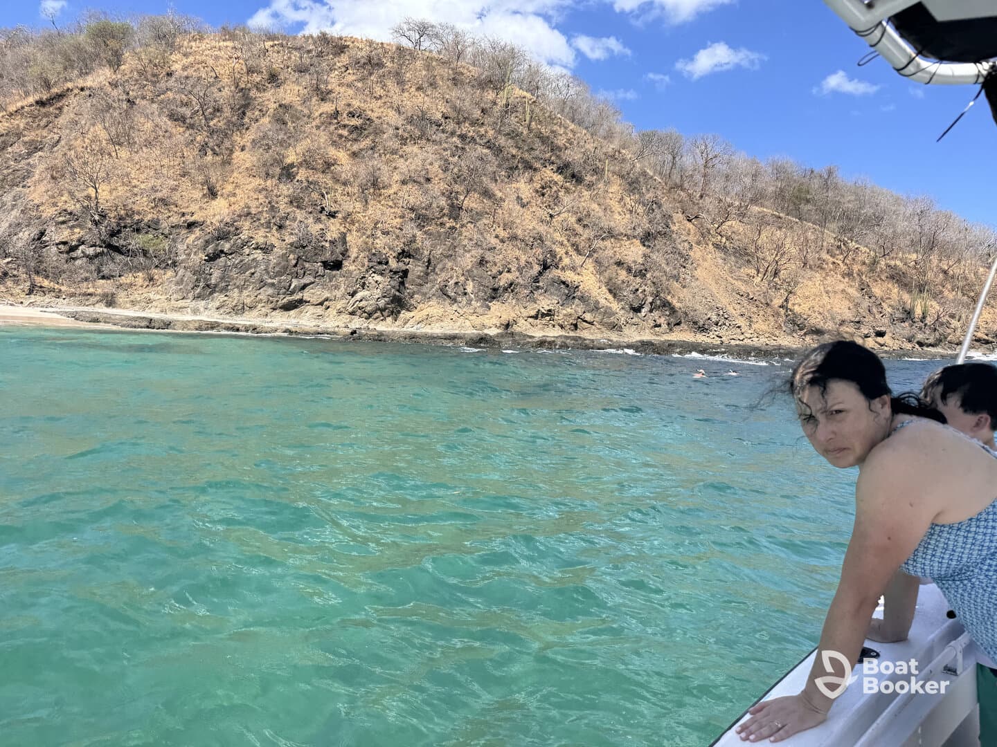 A woman leans over the side of a boat, enjoying the clear turquoise waters and rocky coastline, capturing the essence of a perfect day on the water.