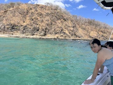 A woman leans over the side of a boat, enjoying the clear turquoise waters and rocky coastline, capturing the essence of a perfect day on the water.