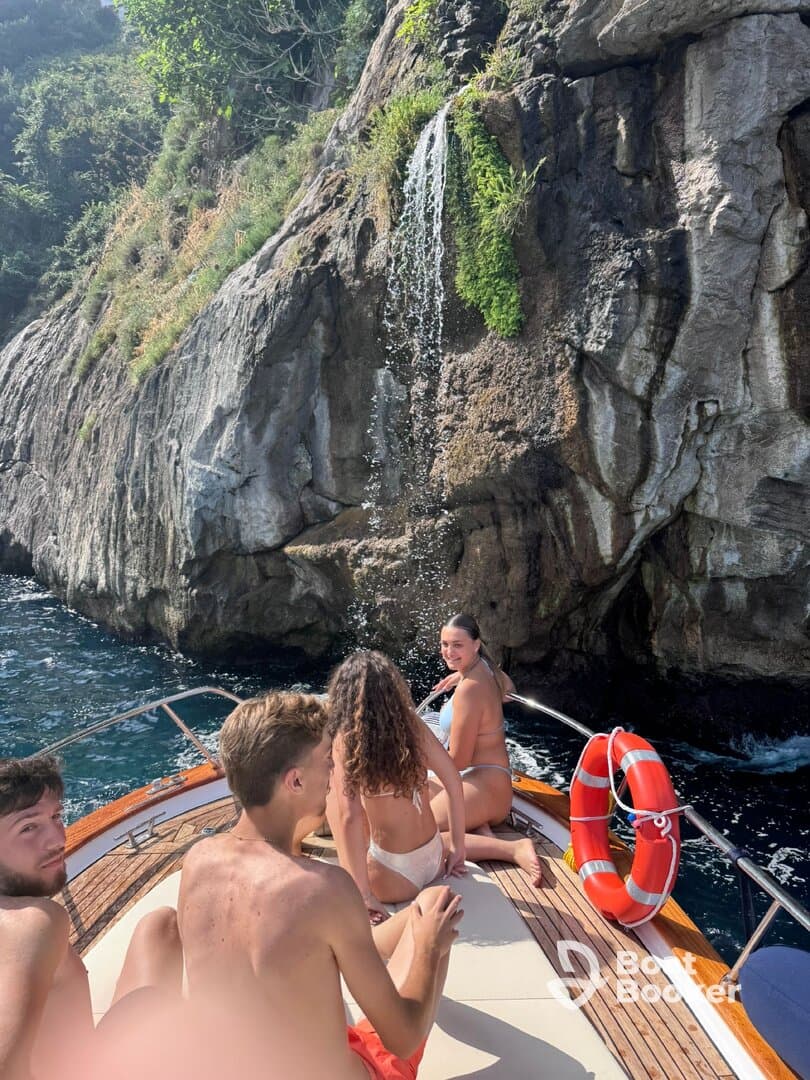 A group of friends enjoys a sunny day on a boat near a stunning waterfall, capturing the essence of summer fun and adventure on the water.