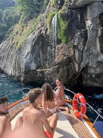 A group of friends enjoys a sunny day on a boat near a stunning waterfall, capturing the essence of summer fun and adventure on the water.