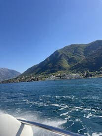 A picturesque view of a coastline with lush mountains in the background, captured from a boat, showcasing the beauty of the landscape and the serene waters.