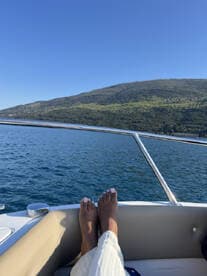 A serene moment on a boat with feet resting on the edge, showcasing the beautiful water and hillside scenery — perfect for relaxation and enjoying the outdoors.